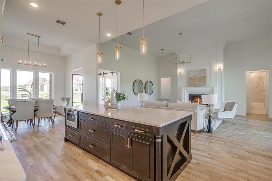 Kitchen featuring light wood-type flooring, a center island, an inviting chandelier, a towering ceiling, and decorative light fixtures