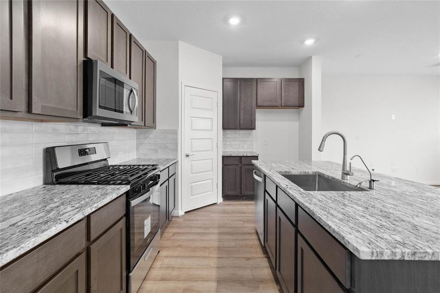 This spacious kitchen features high ceilings, stained wood cabinets, granite countertops, SS appliances, modern tile backsplash, recessed lighting, huge granite kitchen island with large single sink and space for breakfast bar, and a pantry all overlooking your huge family room.