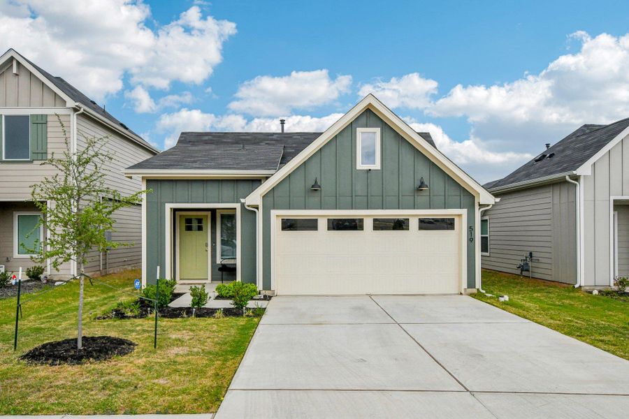 View of front facade with board and batten siding, a front yard, driveway, and a shingled roof