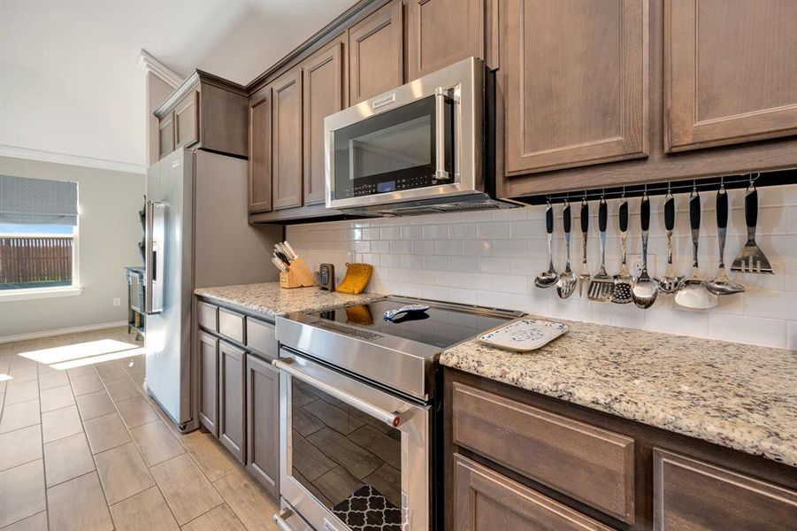 Kitchen with high quality appliances, light stone countertops, backsplash, and dark brown cabinets