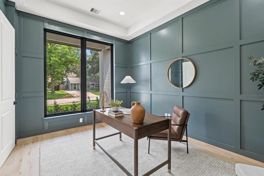 Modern home office with custom paneled walls, and a view of the front yard through large windows.