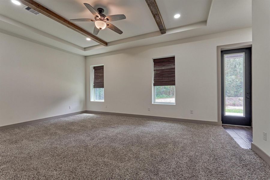 Primary bedroom w/ Frieze carpet, tray ceiling with wood beams and direct access to back porch.  Perfect for sipping your morning coffee and listening to the birds