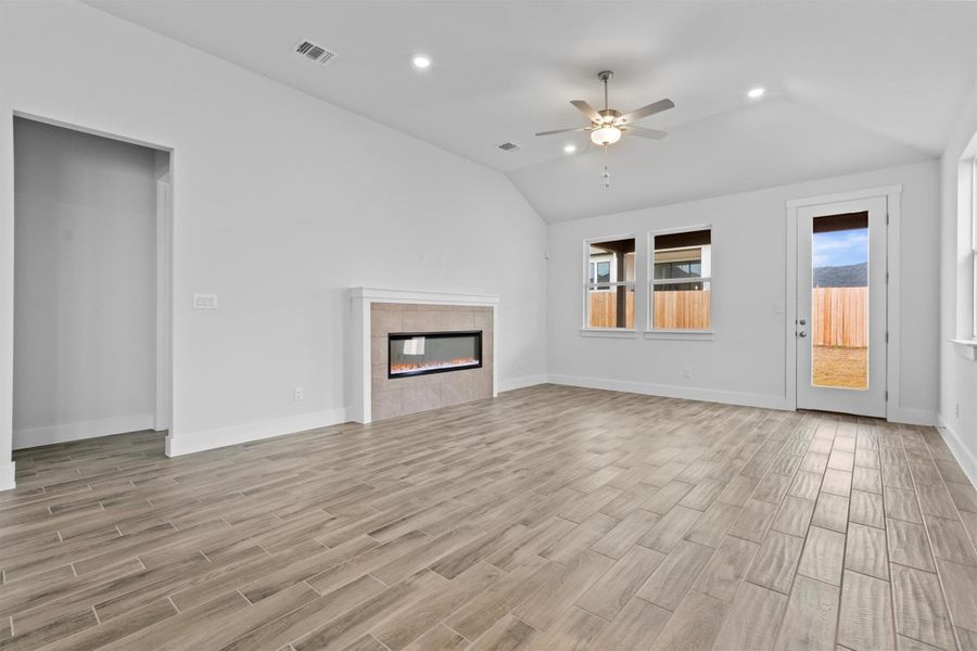 Unfurnished living room featuring ceiling fan, a tiled fireplace, and vaulted ceiling