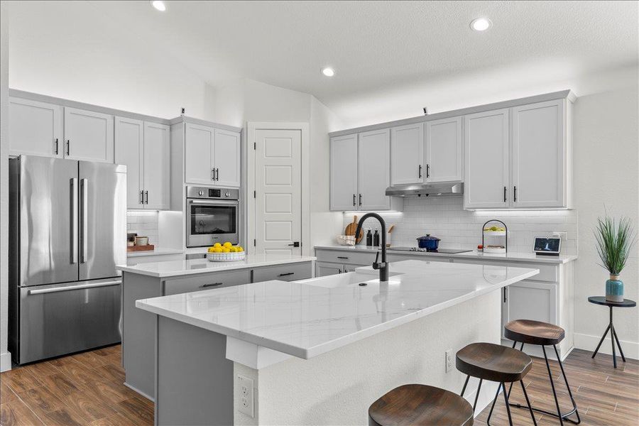 Kitchen featuring appliances with stainless steel finishes, light stone counters, dark wood finished floors, backsplash, and a breakfast bar