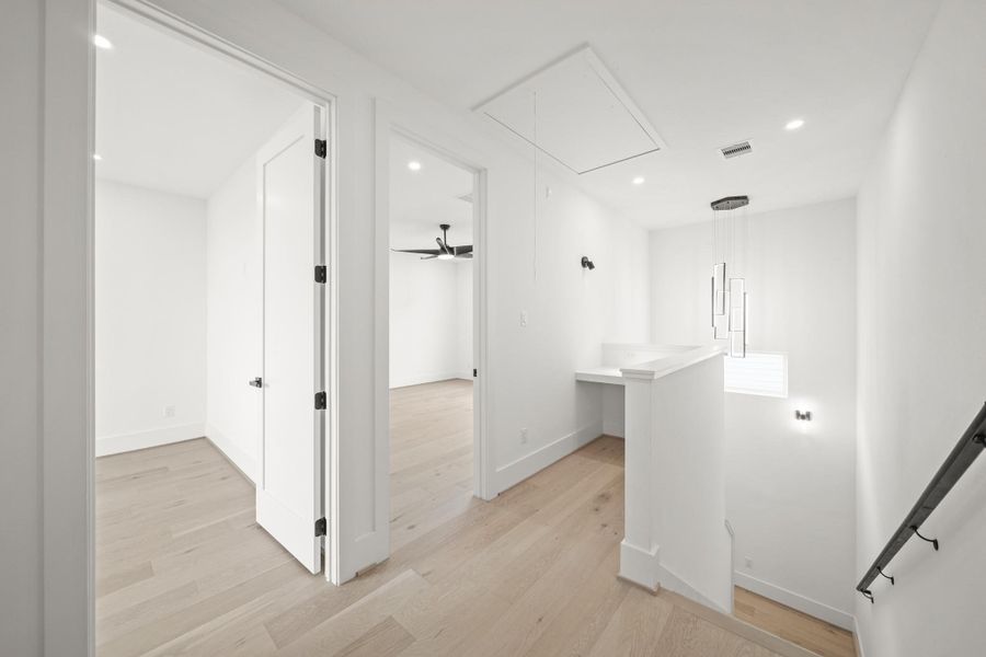 Just outside the primary bedroom is a built-in desk with hardwood floors overlooking the stairwell with sconce lighting and a decorative chandelier.