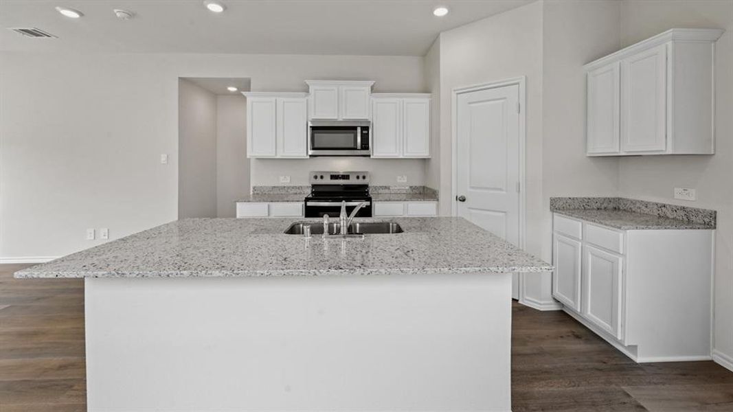 Spacious kitchen featuring a large island with an undermount sink, ample white cabinetry, stone countertops, and wood-finish flooring