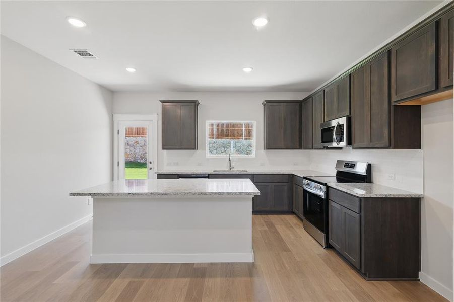 Kitchen featuring stainless steel appliances, dark wood finish cabinetry, light stone counters, light wood-style flooring, and recessed lighting