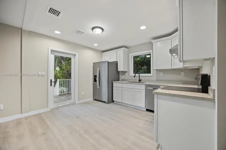 Kitchen featuring white cabinetry, stone-finish countertops, stainless steel appliances, a deep-basin sink with a matte black faucet, and wood-finish flooring Kitchen featuring white cabinetry, stone-finish countertops, stainless steel appliances, a deep-basin sink with a matte black faucet, and wood-finish flooring