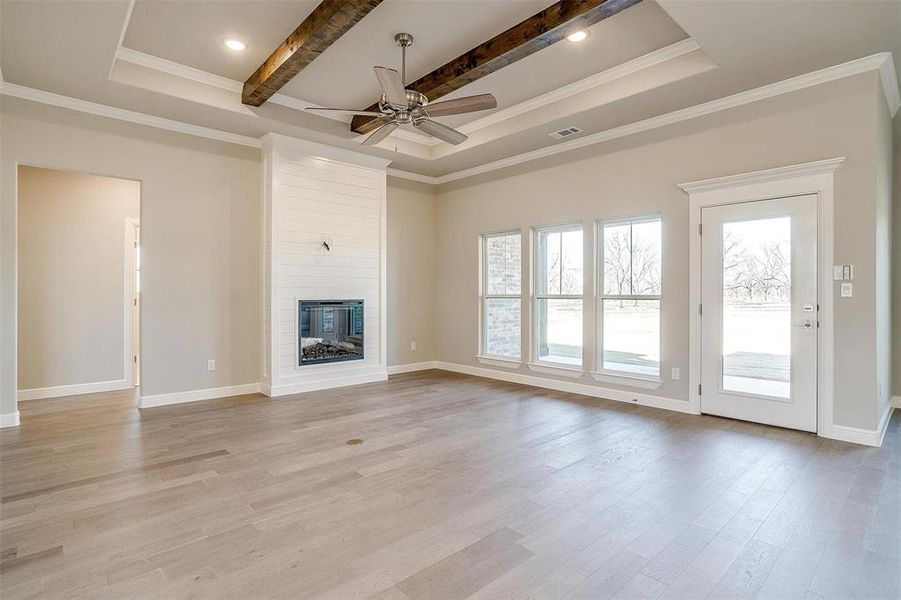 Unfurnished living room with a raised ceiling, crown molding, a fireplace, and light hardwood / wood-style flooring