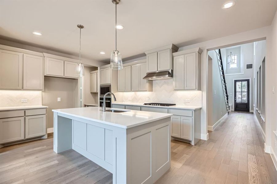 Kitchen featuring decorative backsplash, a center island with sink, recessed lighting, light wood finished floors, and ventilation hood