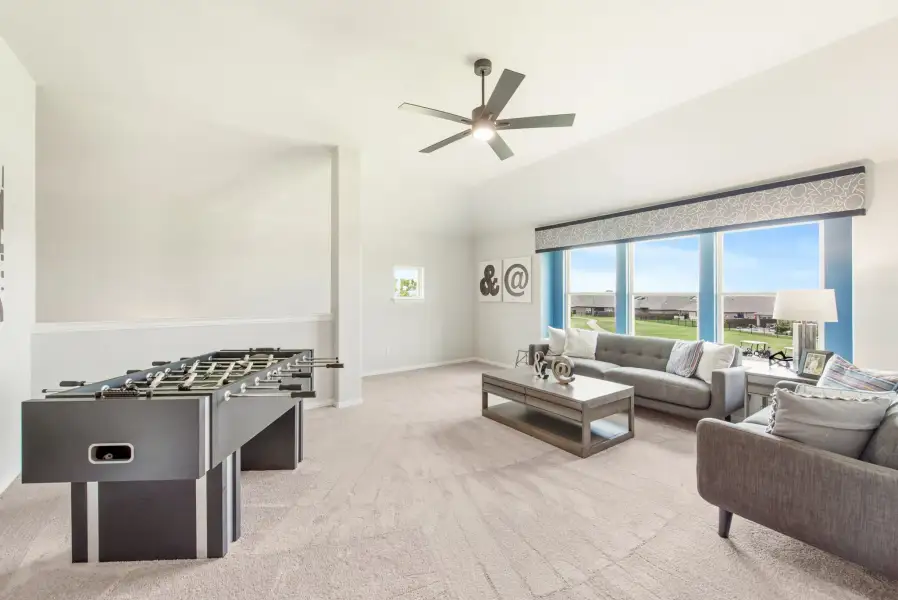 Game room with foosball table, gray sofas, vaulted ceiling with fan, and large windows overlooking backyard