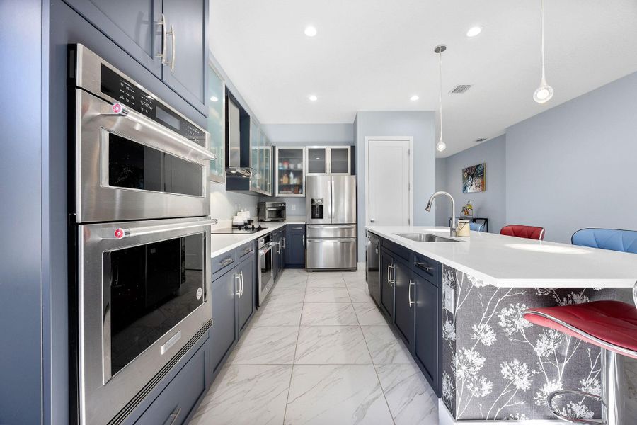 Kitchen featuring stainless steel appliances, glass insert cabinets, decorative light fixtures, a breakfast bar area, and light marble finish floors