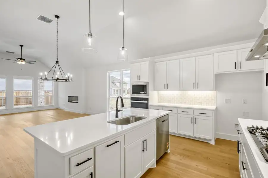 Kitchen featuring white cabinets, a center island with sink, backsplash, light wood-style floors, and suspended lighting