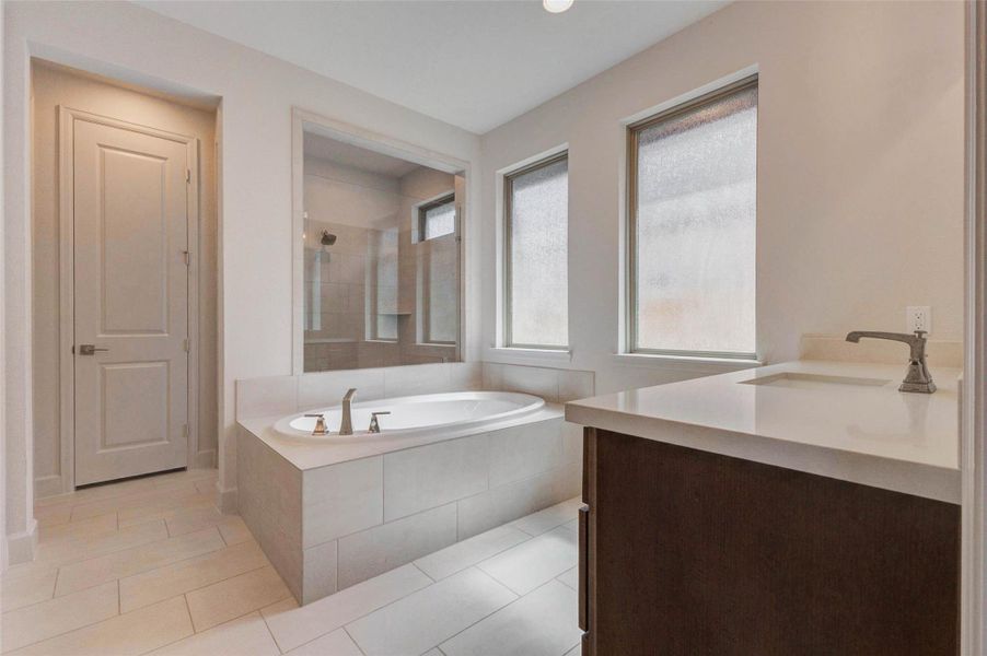 Main bathroom features a spacious soaking tub set against large frosted windows, offering both natural light and privacy. The room includes sleek tile flooring, a stylish vanity with a single sink, and a separate shower area. Main bathroom features a spacious soaking tub set against large frosted windows, offering both natural light and privacy. The room includes sleek tile flooring, a stylish vanity with a single sink, and a separate shower area.