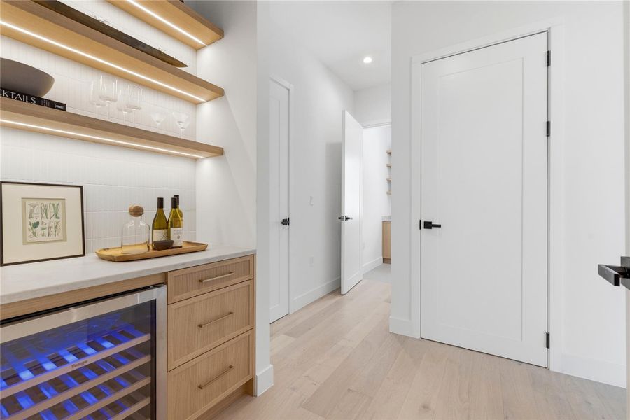Indoor dry bar with wine cooler, light wood finished floors, open shelves, recessed lighting, and tasteful backsplash