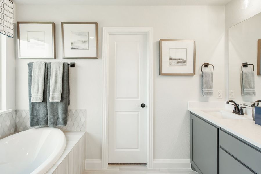 Bathroom with soaking tub, gray vanity cabinets, white countertop, and framed wall art