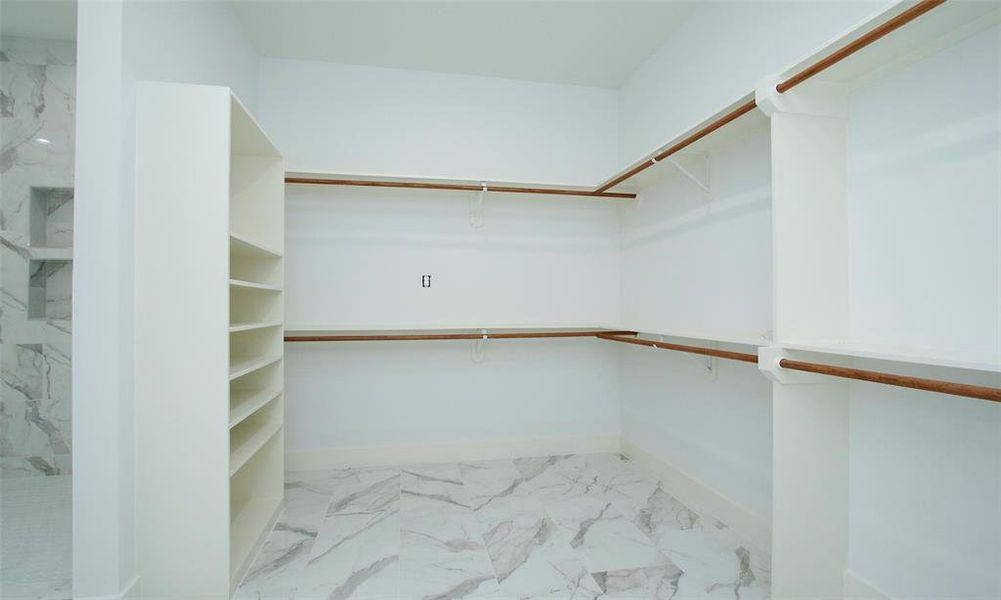 Spacious, clean, and well-organized walk-in closet featuring white shelving, multiple hanging rods with wooden accents, and a marble-patterned tile floor. Perfect for keeping your wardrobe neatly stored.