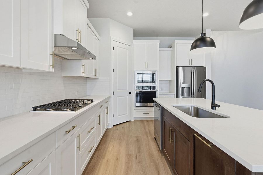 Kitchen featuring light wood-type flooring, stainless steel appliances, pendant lighting, two tone color scheme, and light stone counters