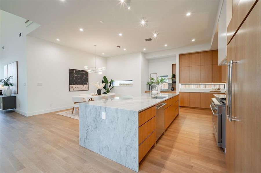 Kitchen featuring appliances with stainless steel finishes, pendant lighting, a large island, light hardwood / wood-style floors, and light stone countertops