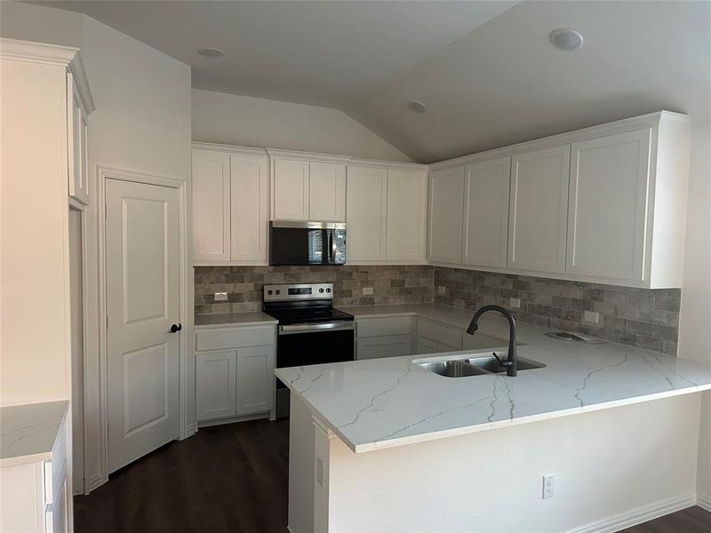 Kitchen featuring white cabinets, stainless steel appliances, light stone countertops, a peninsula, and tasteful backsplash