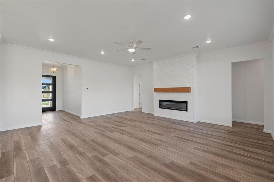 Unfurnished living room featuring ornamental molding, wood finished floors, a large fireplace, recessed lighting, and a ceiling fan