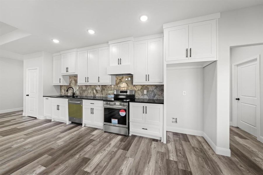Kitchen with stainless steel appliances, white cabinets, dark countertops, recessed lighting, and light wood-style flooring Kitchen with stainless steel appliances, white cabinets, dark countertops, recessed lighting, and light wood-style flooring