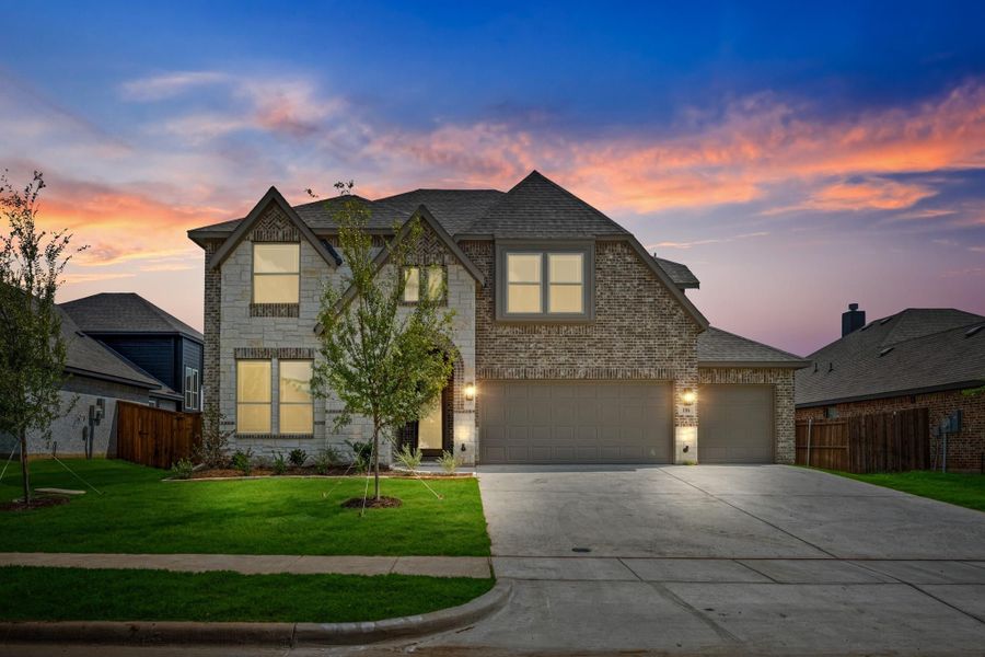 Two-story brick home with three-car garage and concrete driveway, photographed at dusk with lights on