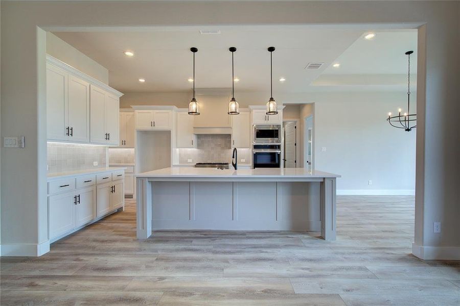 Kitchen featuring light hardwood / wood-style floors, stainless steel appliances, a spacious island, tasteful backsplash, and white cabinetry