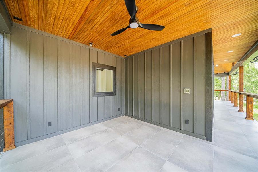 Covered outdoor living area featuring a natural wood-finish ceiling, board and batten wall siding, a contemporary ceiling fan, recessed lighting, and large format tile flooring