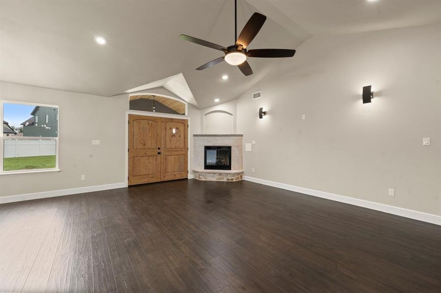 Unfurnished living room with lofted ceiling, ceiling fan, wood finished floors, baseboards, and a stone fireplace