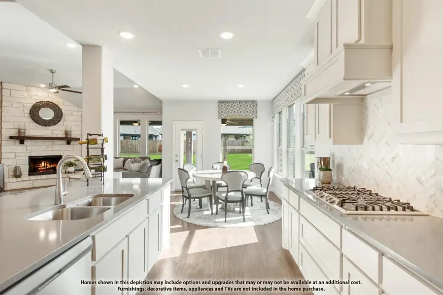 Open kitchen with white cabinets, gas cooktop, and herringbone backsplash, overlooking a dining area and living room with stone fireplace.