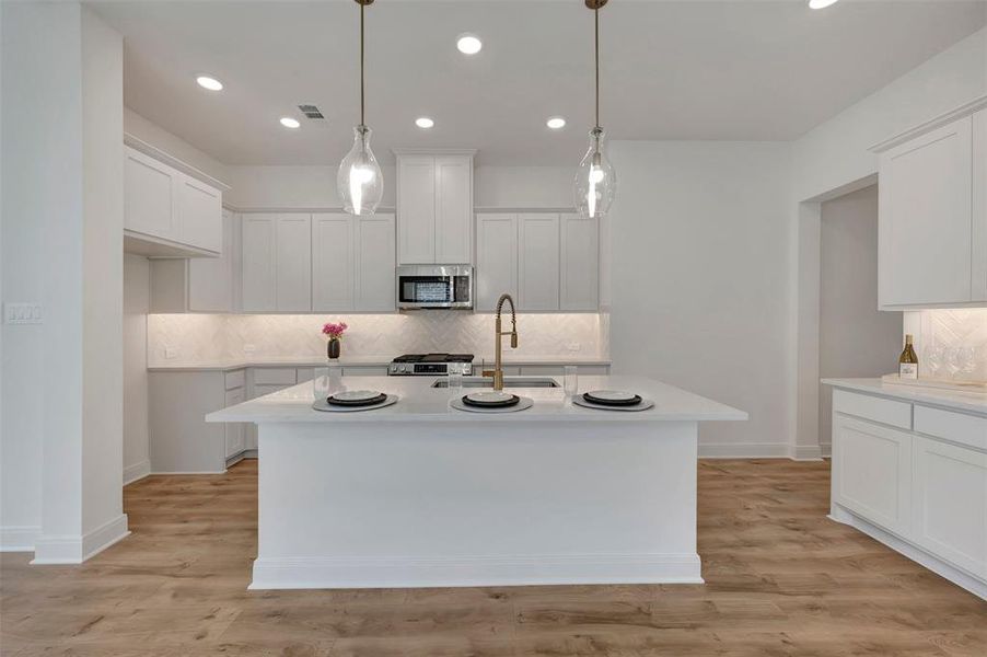 Modern kitchen featuring an expansive center island with seating, white shaker-style cabinetry, and wood-finish flooring