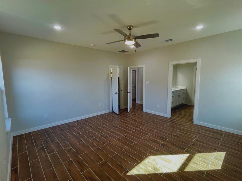 Unfurnished bedroom with dark wood-type flooring, ceiling fan, and ensuite bathroom