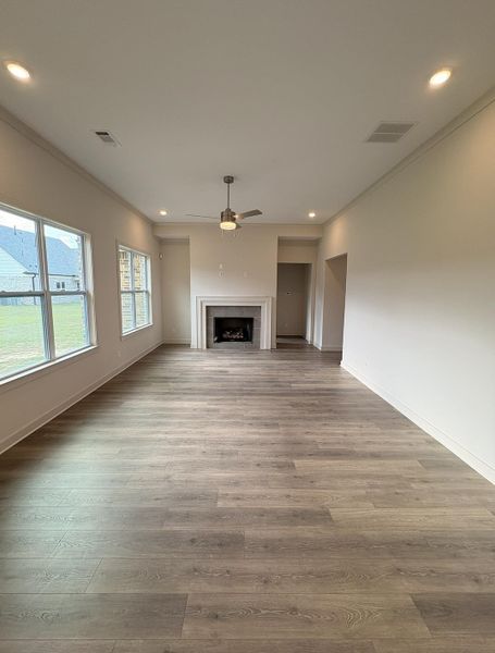 Spacious living area featuring wood-finish flooring, a decorative fireplace with a mantel, multiple windows, recessed lighting, and a ceiling fan