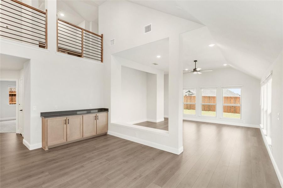 Open living area with vaulted ceiling, hardwood floors, built-in cabinet, and second-floor railing overlook Open living area with vaulted ceiling, hardwood floors, built-in cabinet, and second-floor railing overlook