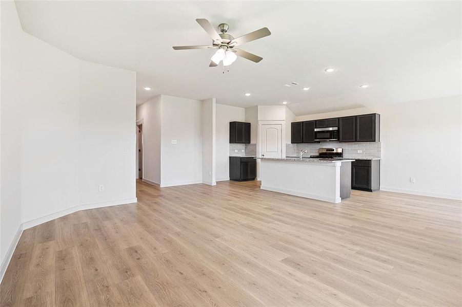 Kitchen featuring light wood-type flooring, ceiling fan, a center island with sink, stainless steel appliances, and backsplash