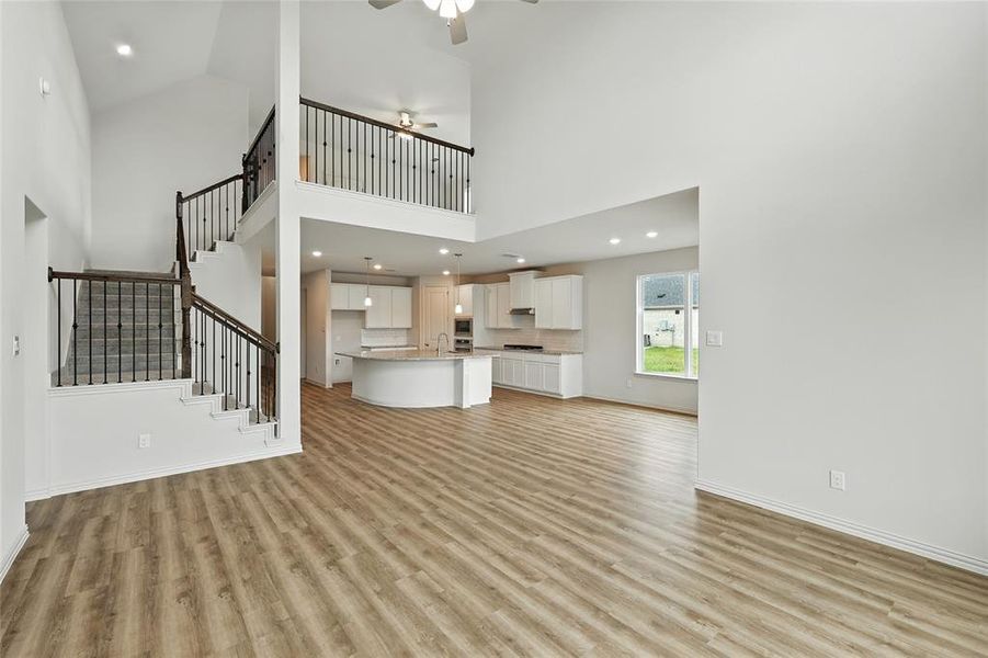 Unfurnished living room featuring ceiling fan, recessed lighting, light wood finished floors, and a high ceiling