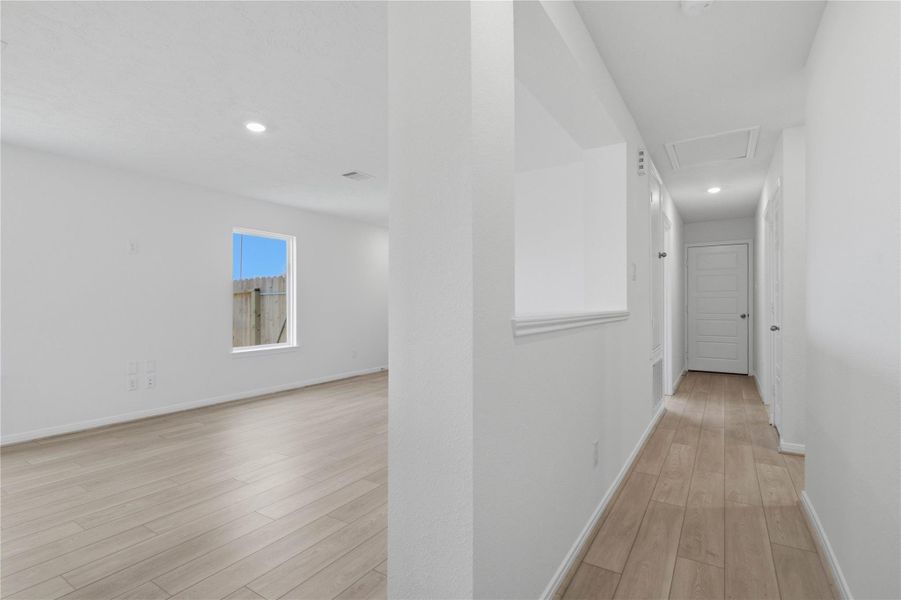 This welcoming hallway provides a private transition from the main living areas to the bedrooms and bathrooms. It continues the home's seamless vinyl plank flooring and features a built-in cutout ledge that looks into the living room, enhancing the open-concept feel while maintaining privacy.