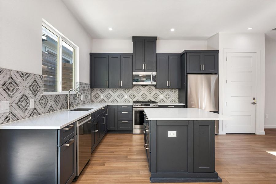 Kitchen with light stone counters, stainless steel appliances, decorative backsplash, a center island, and light wood finished floors