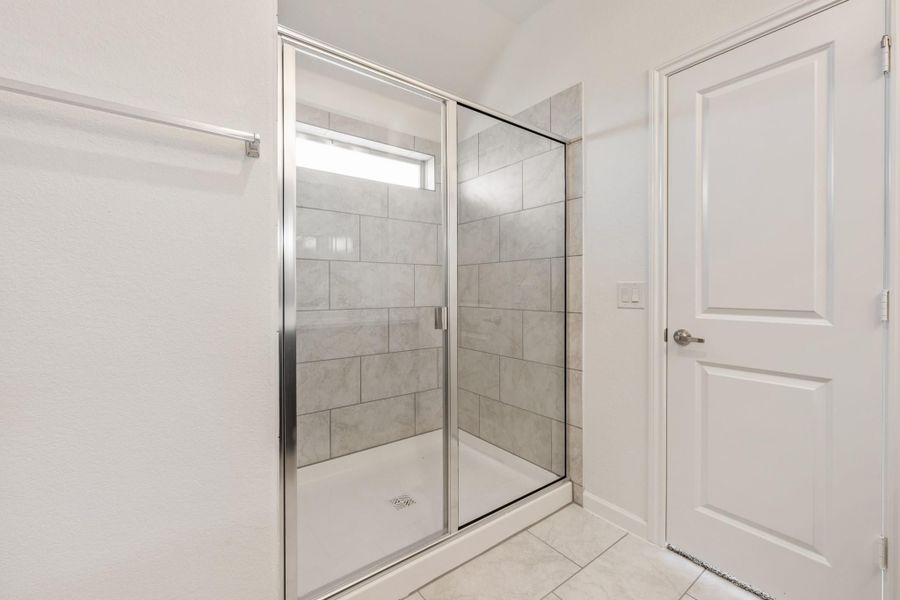 Walk-in shower with glass sliding door, gray tile walls, and white tile floor in a bathroom