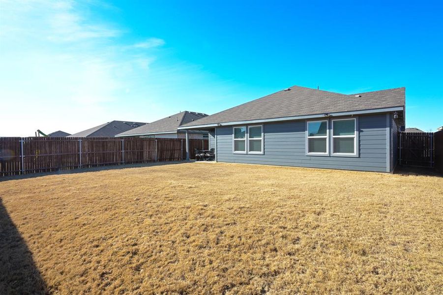Back of property with a shingled roof, a lawn, and a fenced backyard