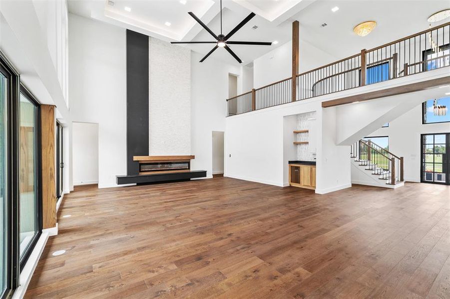 Unfurnished living room with a towering ceiling, ceiling fan, hardwood / wood-style floors, and a fireplace