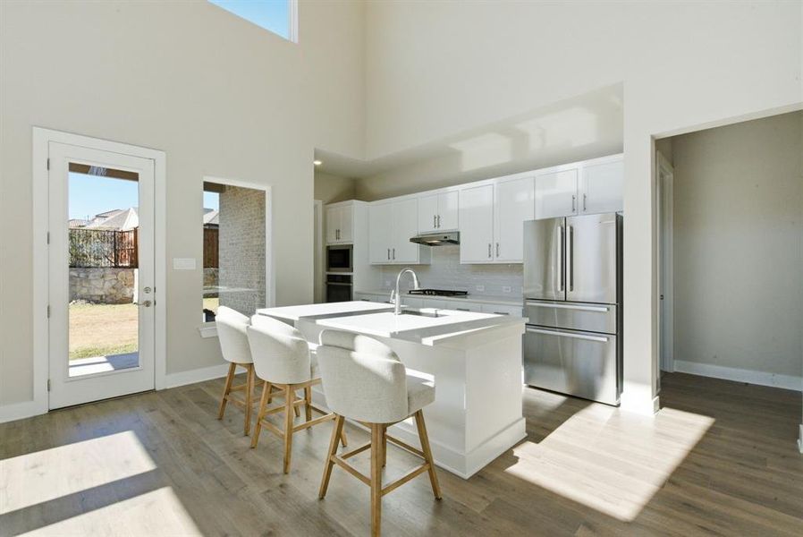 Kitchen featuring white cabinetry, stainless steel appliances, an island with sink, a breakfast bar, and light wood-style flooring
