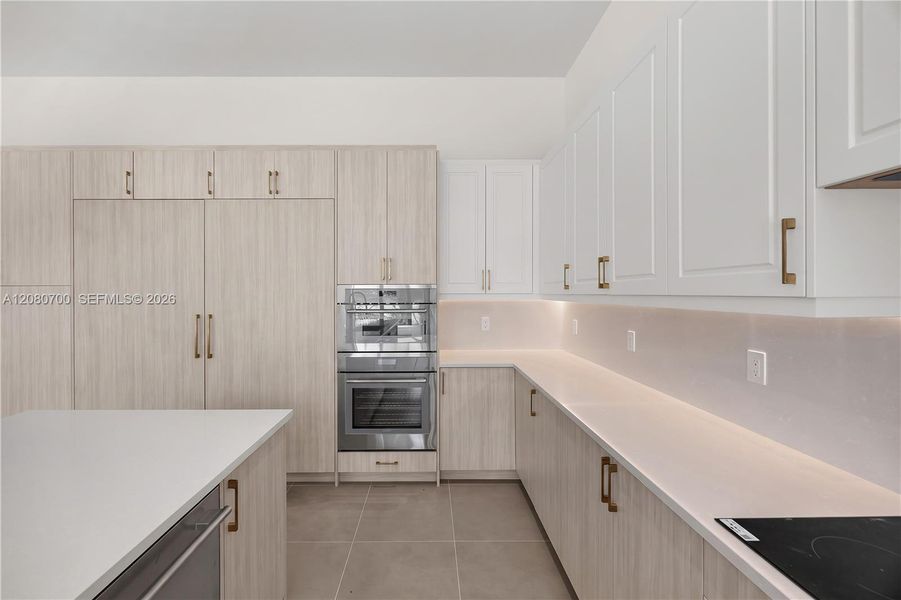 Kitchen featuring light wood-finish lower cabinetry, white upper cabinetry, stainless steel double ovens, an integrated refrigerator, and light-toned countertops