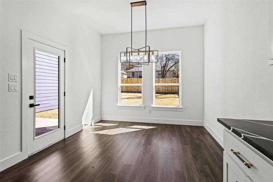 Unfurnished dining area featuring dark wood finished floors, a wealth of natural light, and baseboards