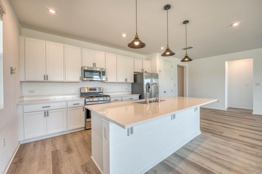An expansive breakfast island anchors this modern culinary space featuring recessed lighting and wood-toned flooring.