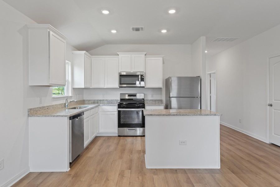 Kitchen with stainless steel appliances, a center island, white cabinetry, light stone counters, and light wood-style floors