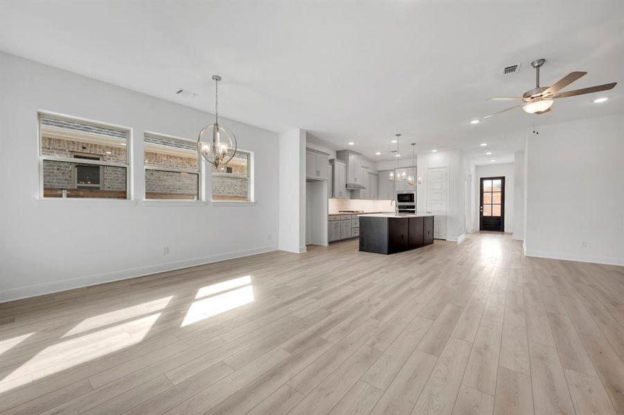 Unfurnished living room with a chandelier, a ceiling fan, and light wood finished floors Unfurnished living room with a chandelier, a ceiling fan, and light wood finished floors