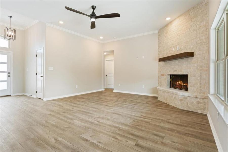 Unfurnished living room featuring healthy amount of natural light, ornamental molding, light wood finished floors, a fireplace, and a chandelier Unfurnished living room featuring healthy amount of natural light, ornamental molding, light wood finished floors, a fireplace, and a chandelier