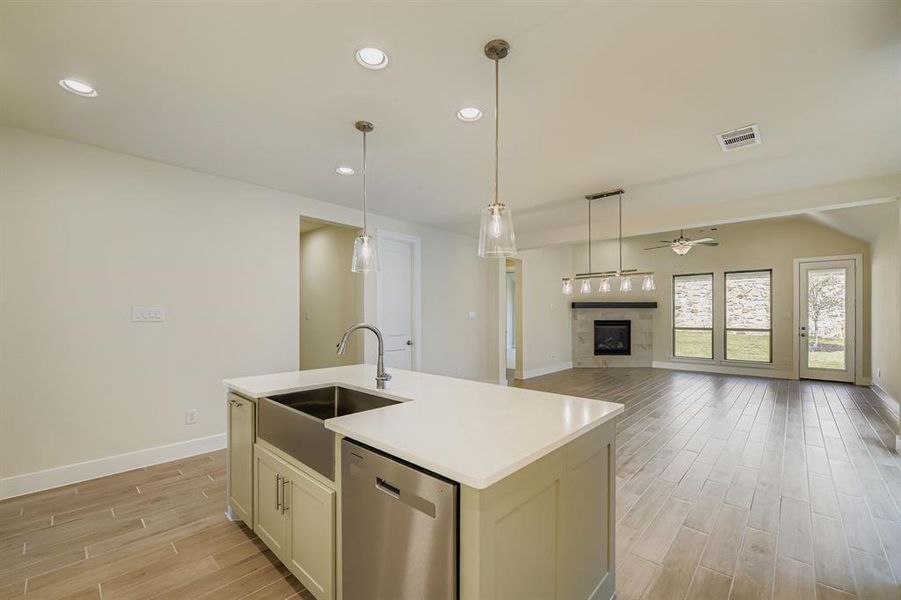 Kitchen with wood finish floors, recessed lighting, stainless steel dishwasher, open floor plan, and a tile fireplace